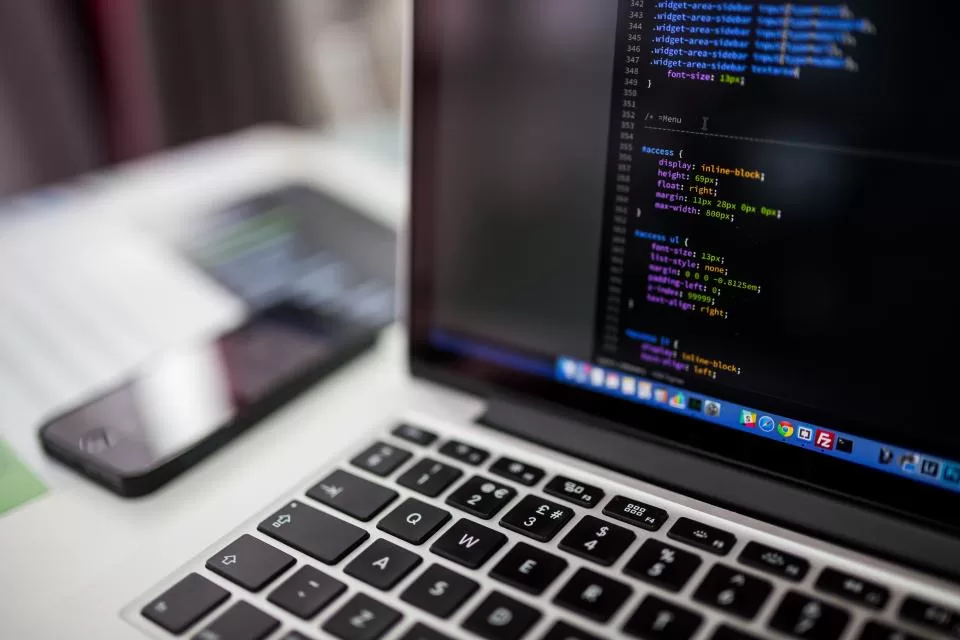 Laptop képernyője programkóddal, mellette egy okostelefon