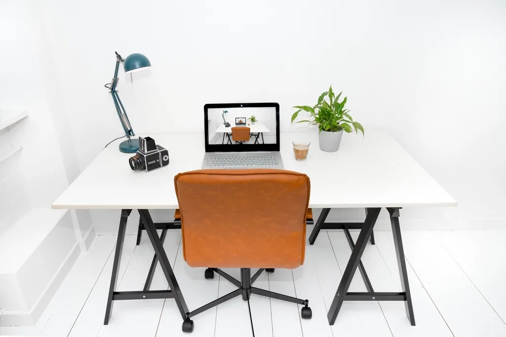 Laptop egy fehér irodai íróasztalon, előtte barna irodai szék