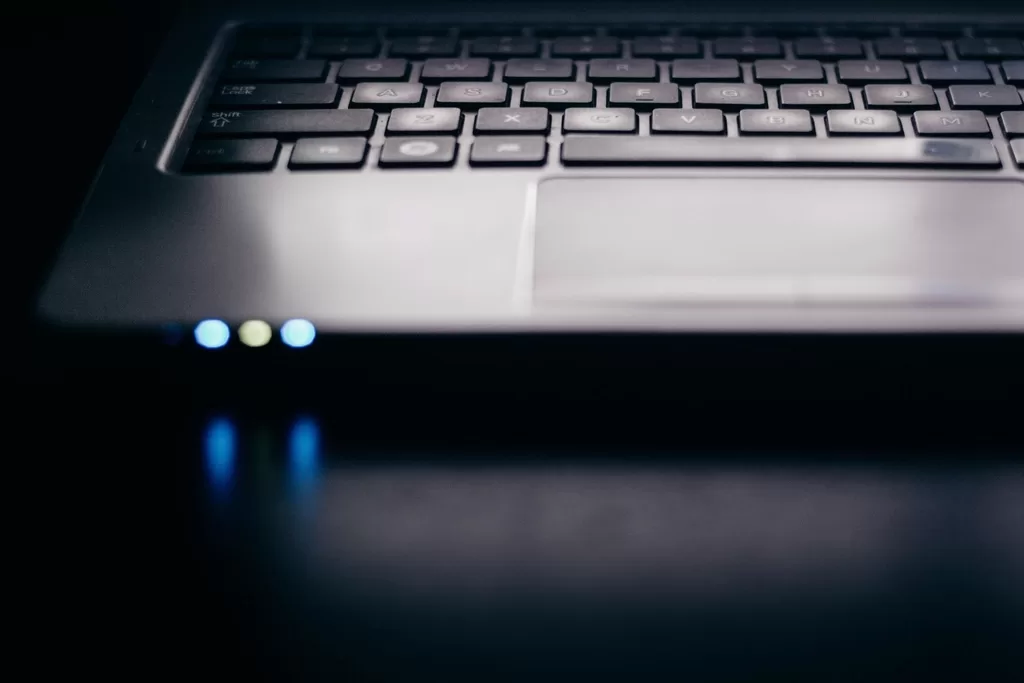 Laptop billentyűzete és érintőpadja közelről, sötét asztalon, világító állapotjelző fényekkel
